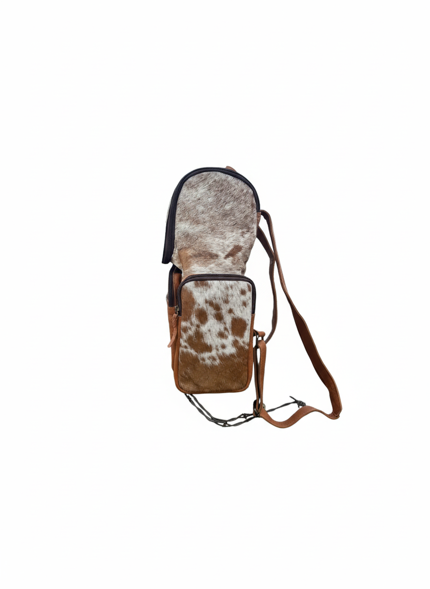 Cow print bag with brown leather strap on a wooden post against a rural background
